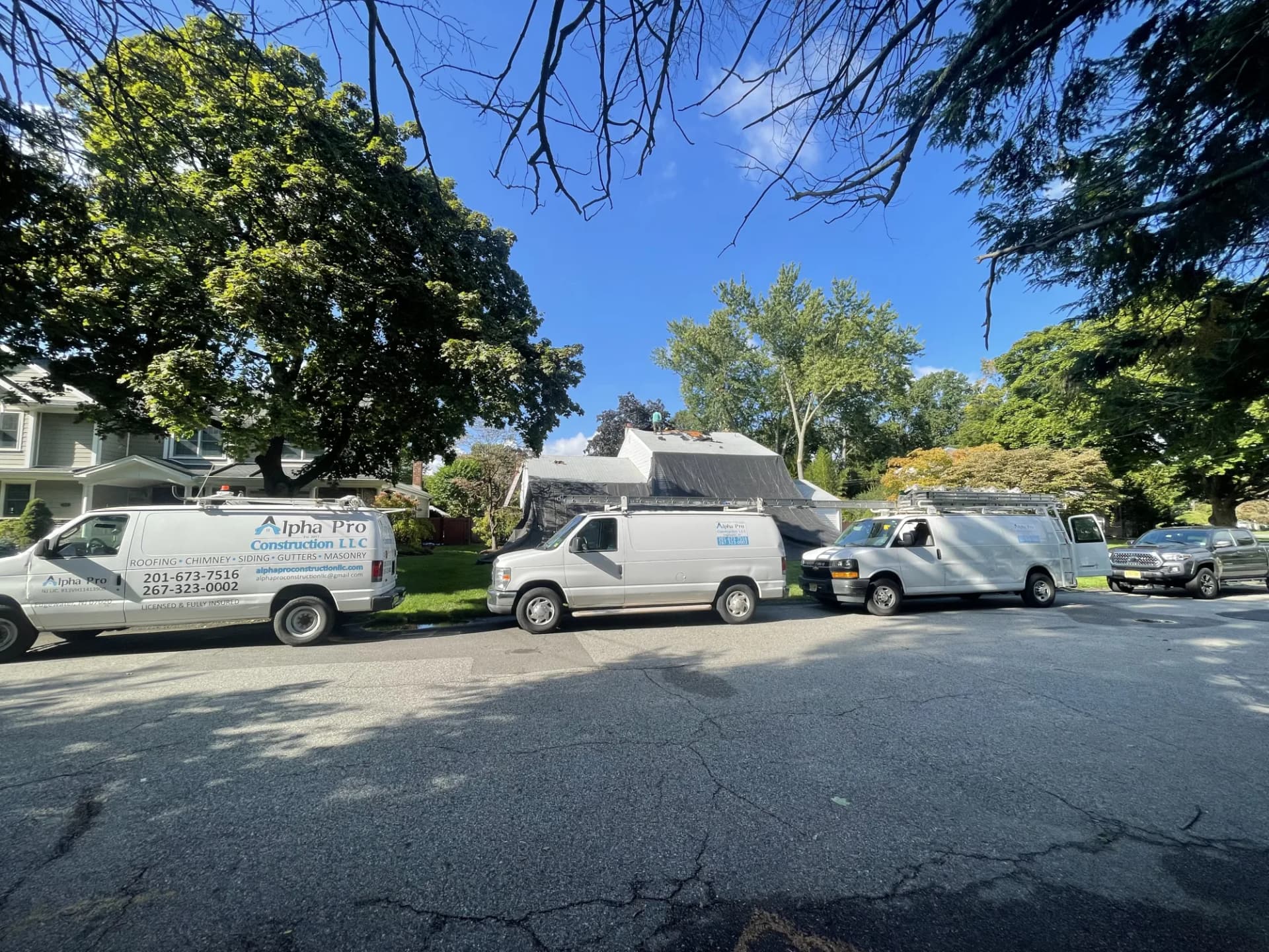 Alpha Pro Construction fleet vans parked outside a residential roofing project in New Jersey