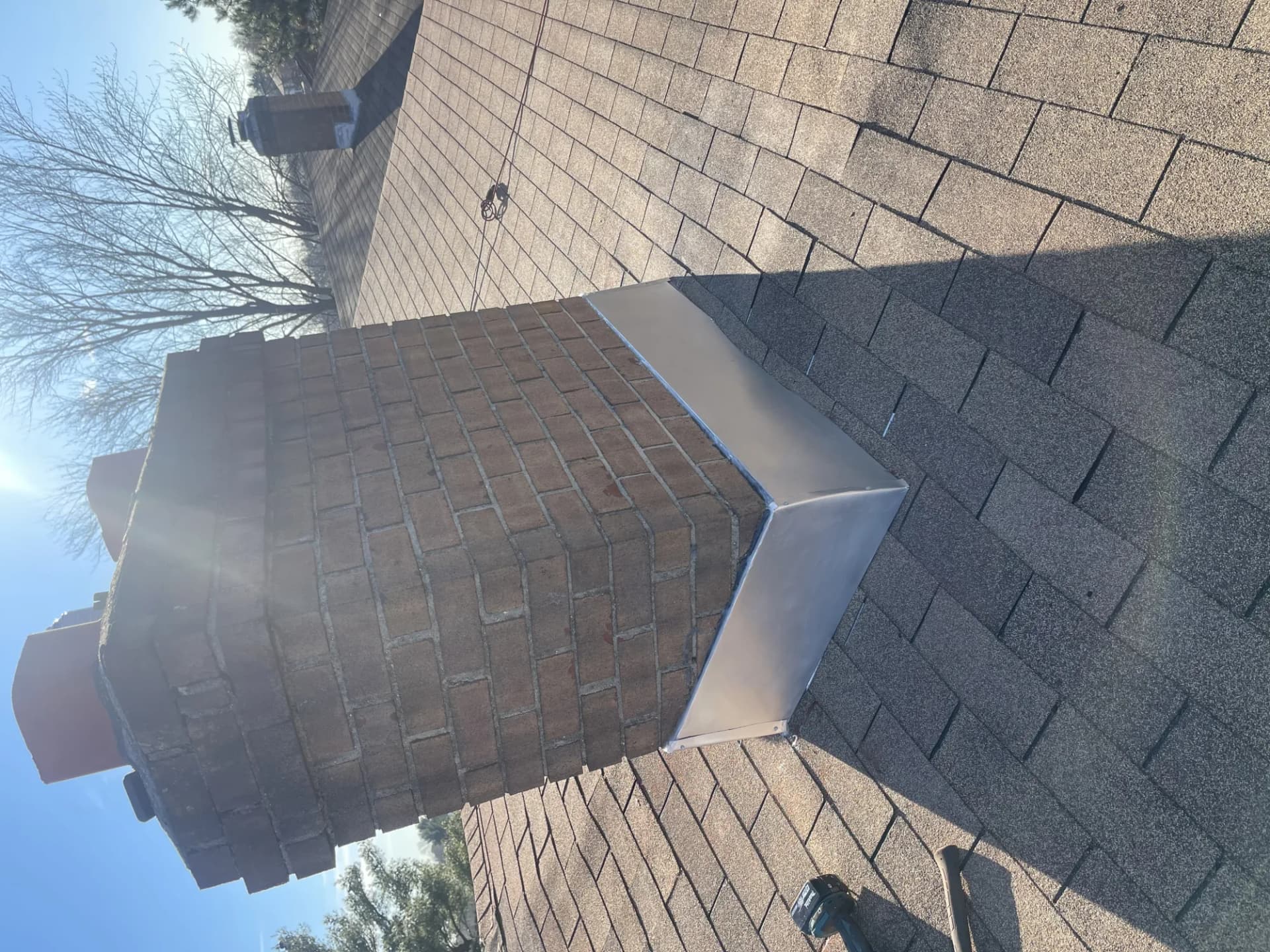Roofer repairing step flashing along a brick chimney on a New Jersey shingle roof