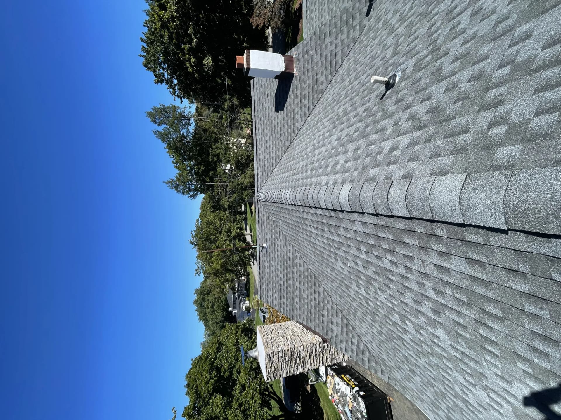 Completed charcoal gray asphalt shingle roof with ridge cap on a residential home under a blue sky in New Jersey
