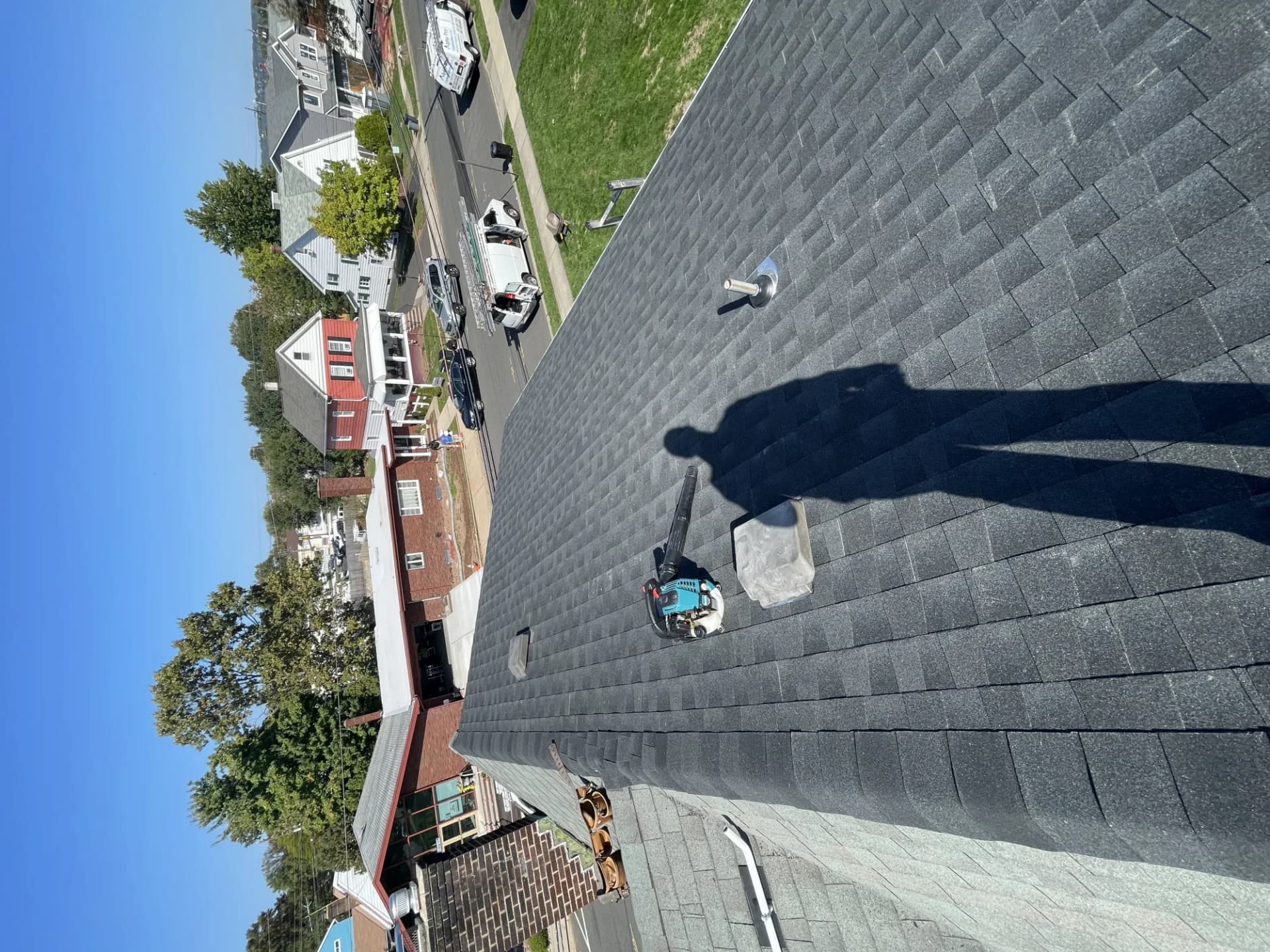 Roofing crew clearing debris off a charcoal shingle roof with a blower in New Jersey