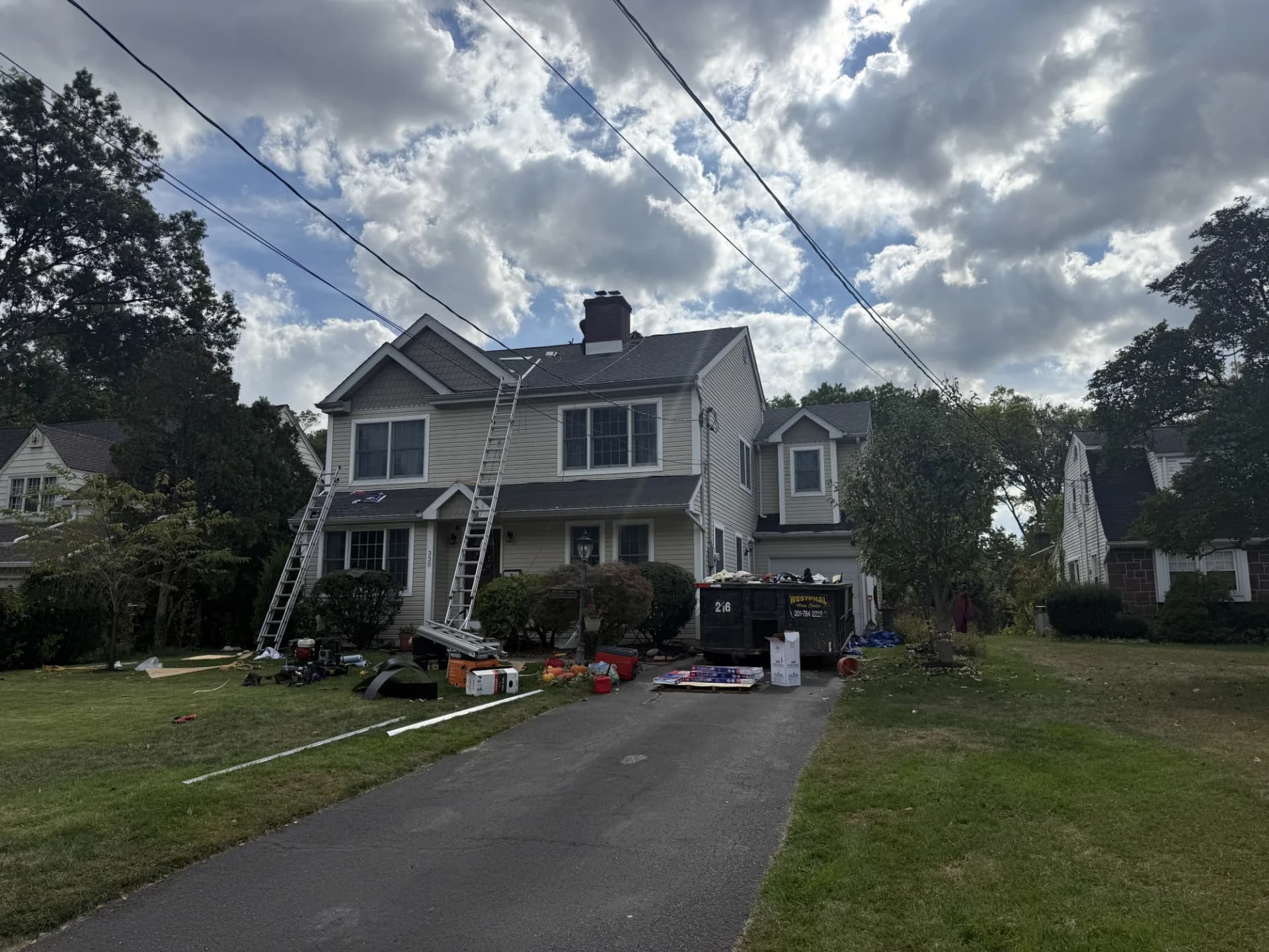 Full roof replacement in progress on a New Jersey colonial home with a debris dumpster in the driveway