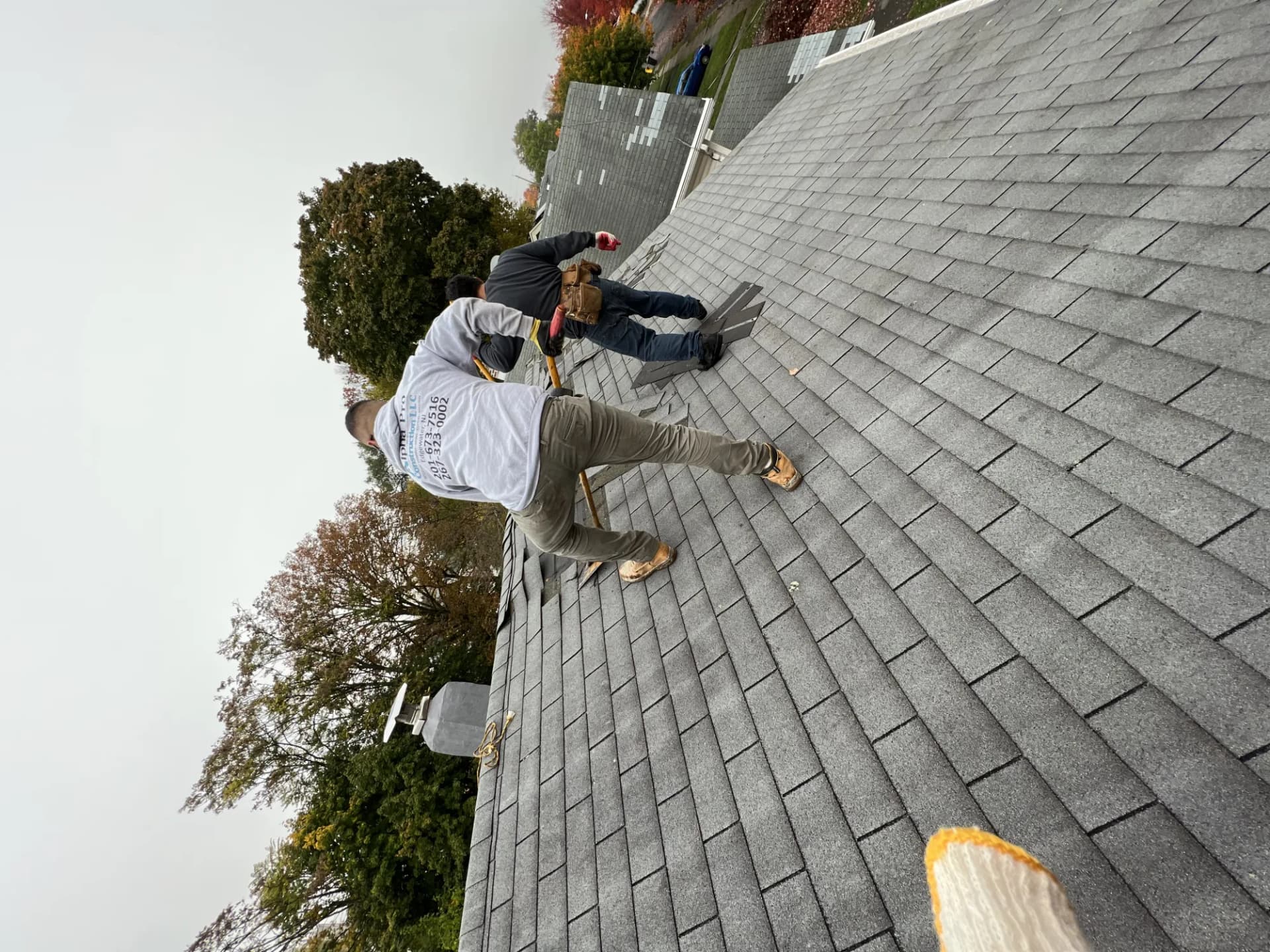 Two-person crew inspecting an aging gray asphalt shingle roof at the ridge on a New Jersey home