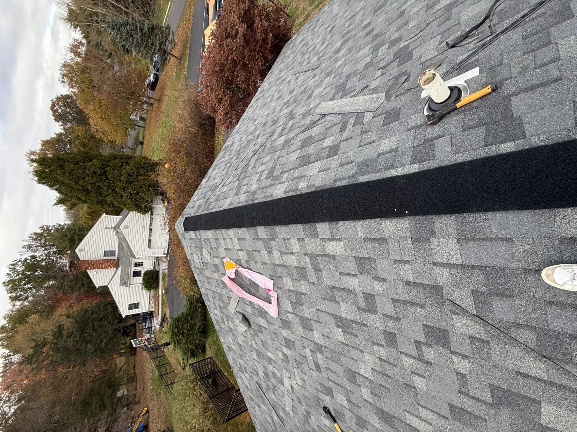 Aerial view of a nearly complete gray asphalt shingle roof with a ridge vent being installed in New Jersey