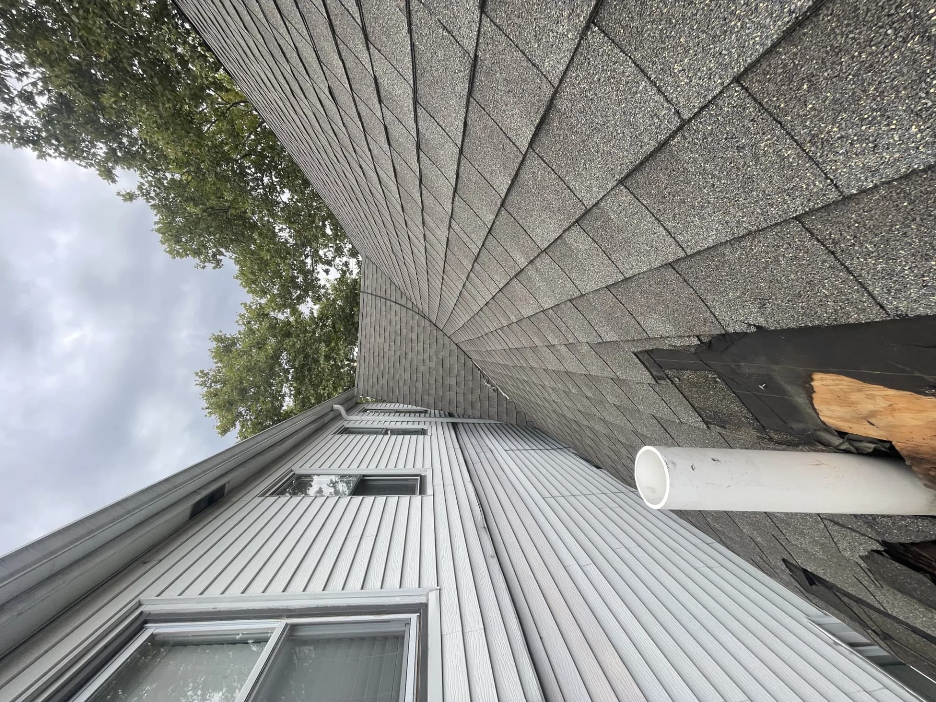 Corner of a residential asphalt shingle roof with storm damage, shingles torn away and bare wood decking exposed in New Jersey