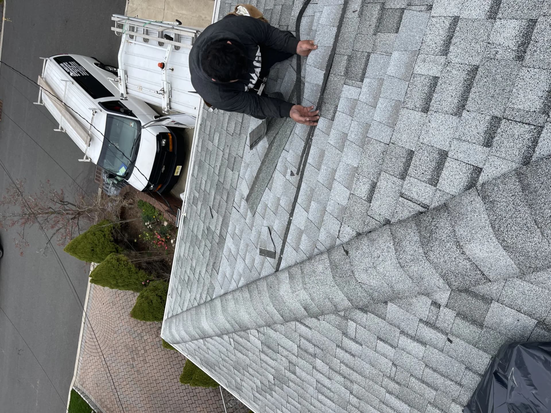 Roofer inspecting the ridge line of a gray asphalt shingle roof on a New Jersey home