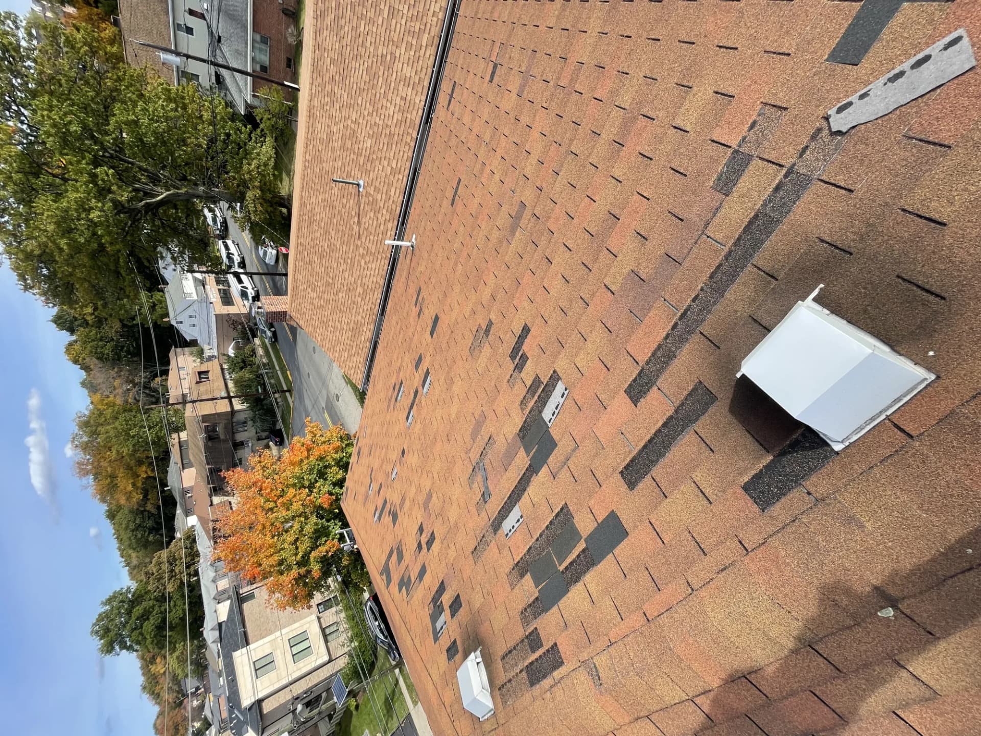 Aerial view of a brown asphalt shingle roof in New Jersey with multiple missing, displaced shingle tabs from storm damage