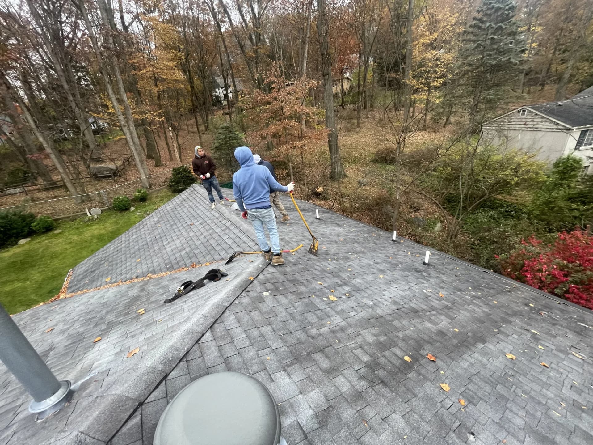 Roofing crew clearing autumn leaves and debris off a gray shingle roof and gutters in New Jersey