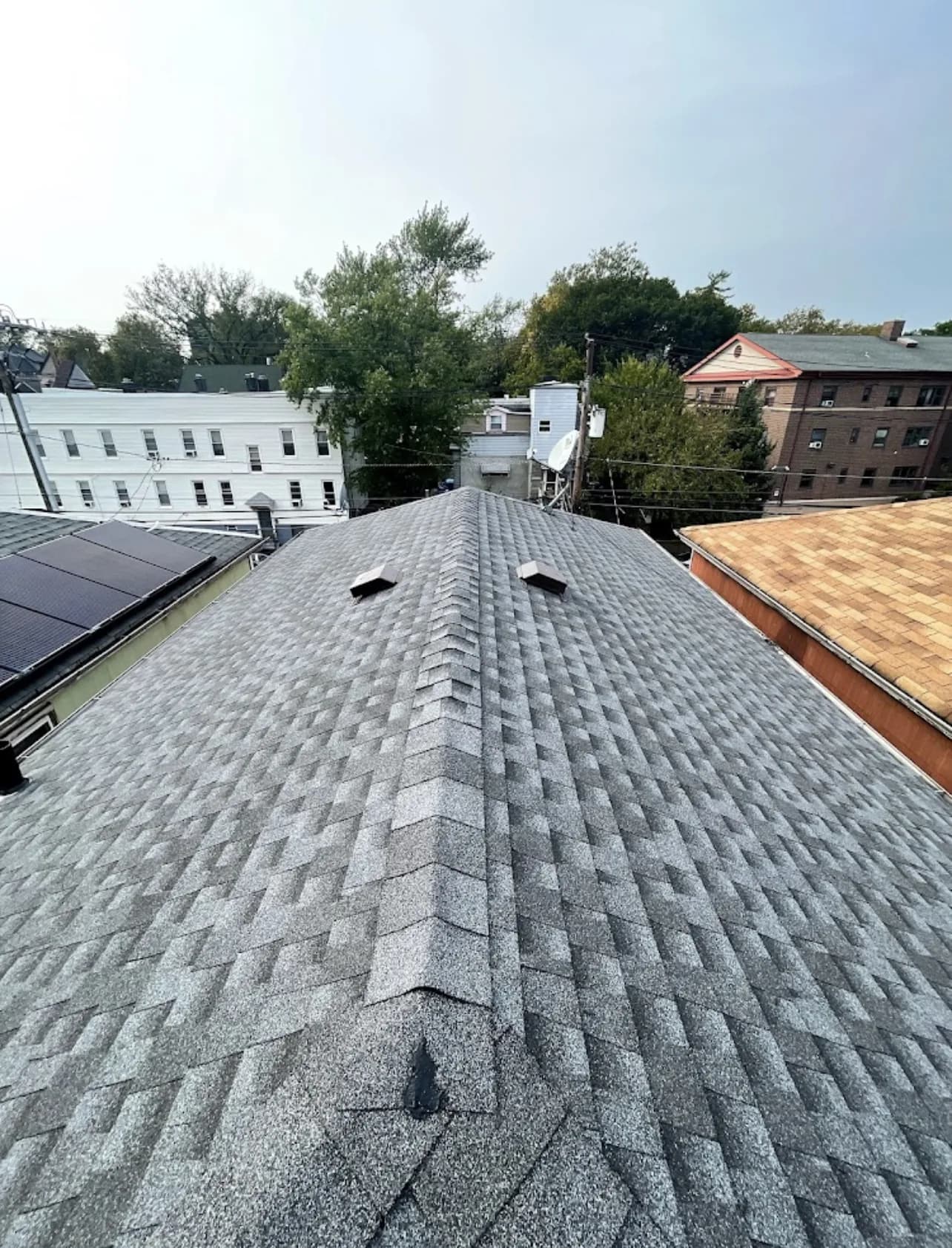 Completed gray asphalt shingle hip roof with box vents on a residential building in an urban New Jersey neighborhood