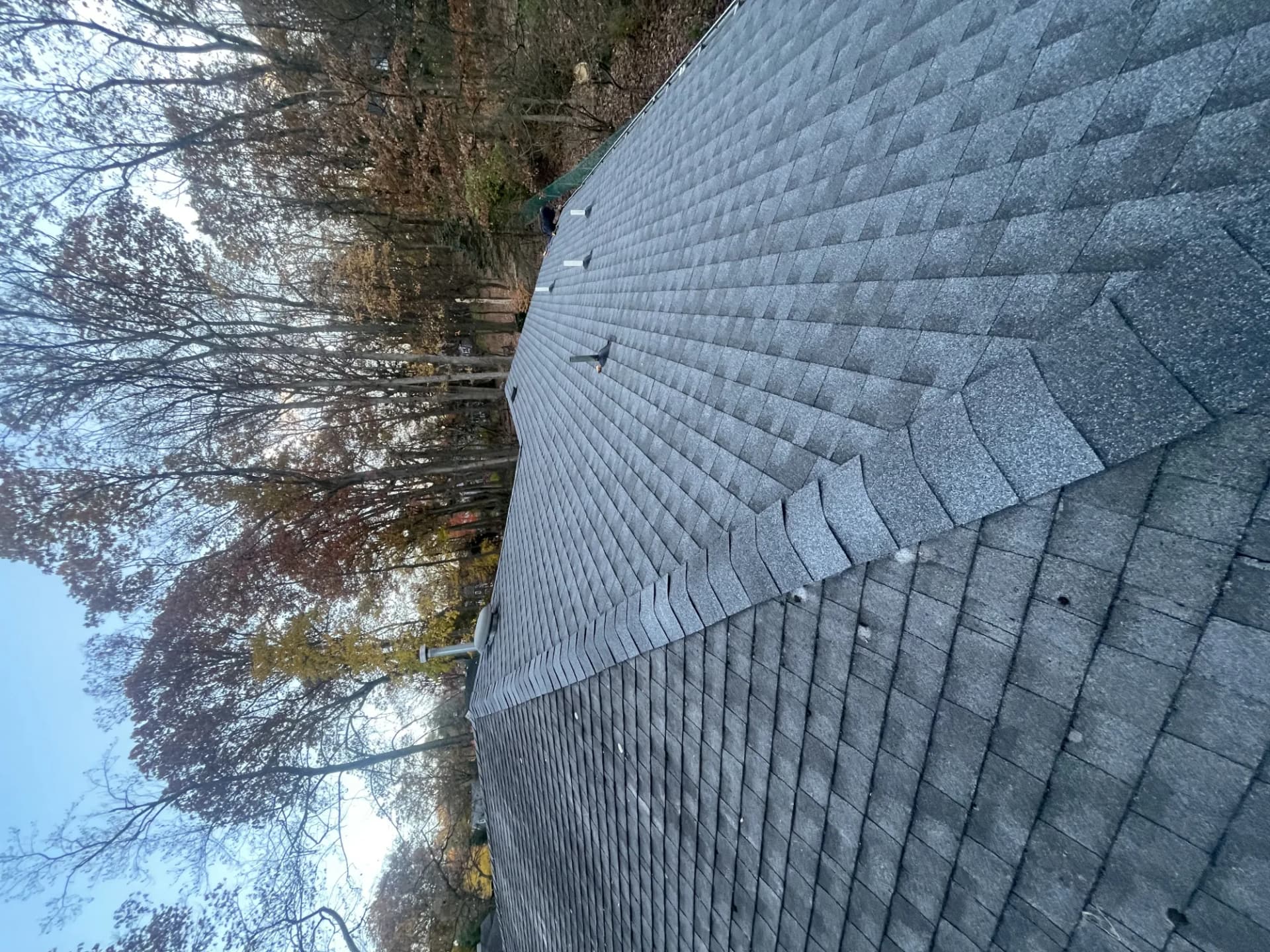 Completed gray asphalt shingle roof showing a clean hip valley and ridge with autumn trees behind it in New Jersey