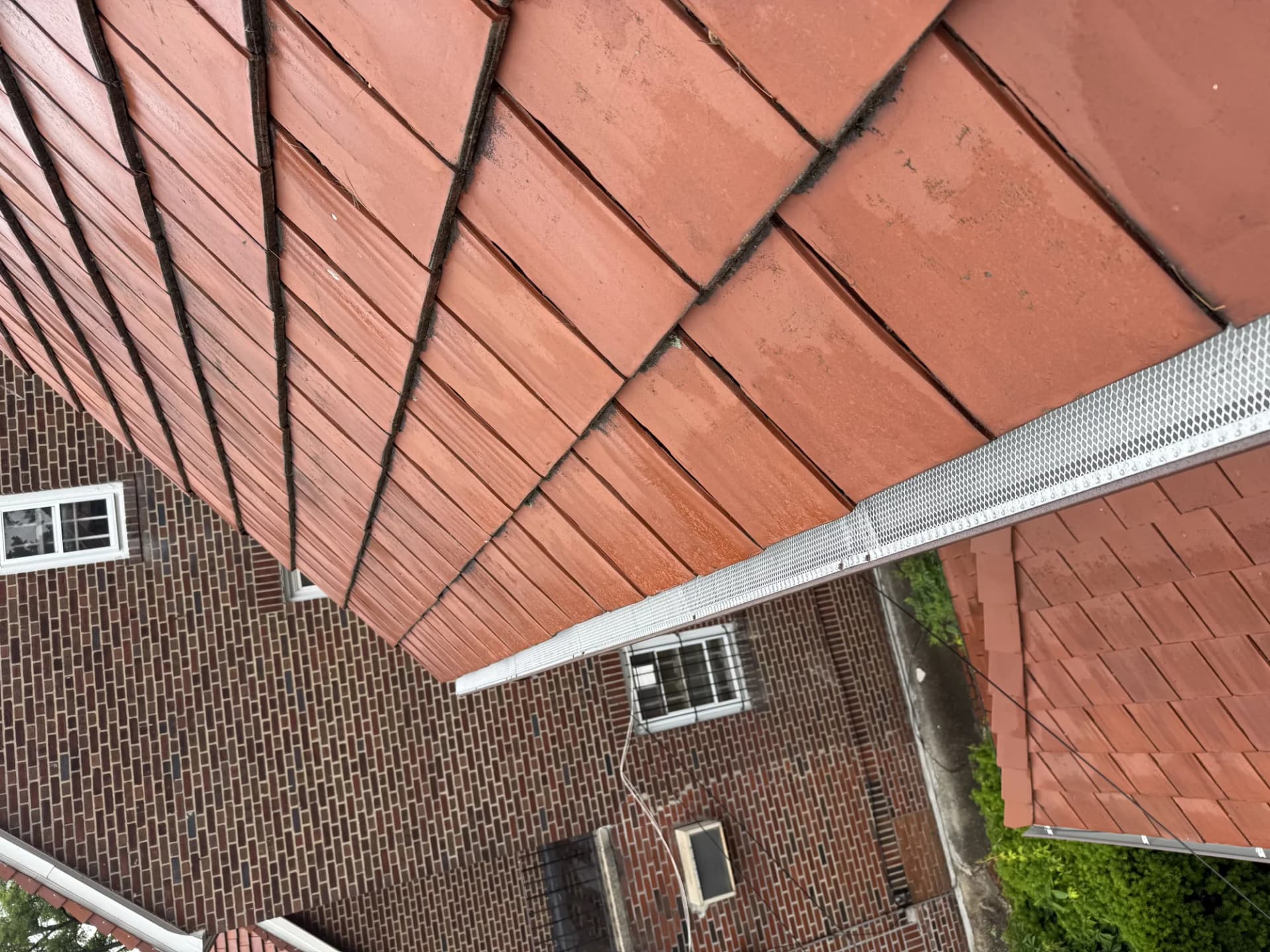 Aerial view of a red clay tile roof with a metal gutter guard on a brick commercial building in New Jersey
