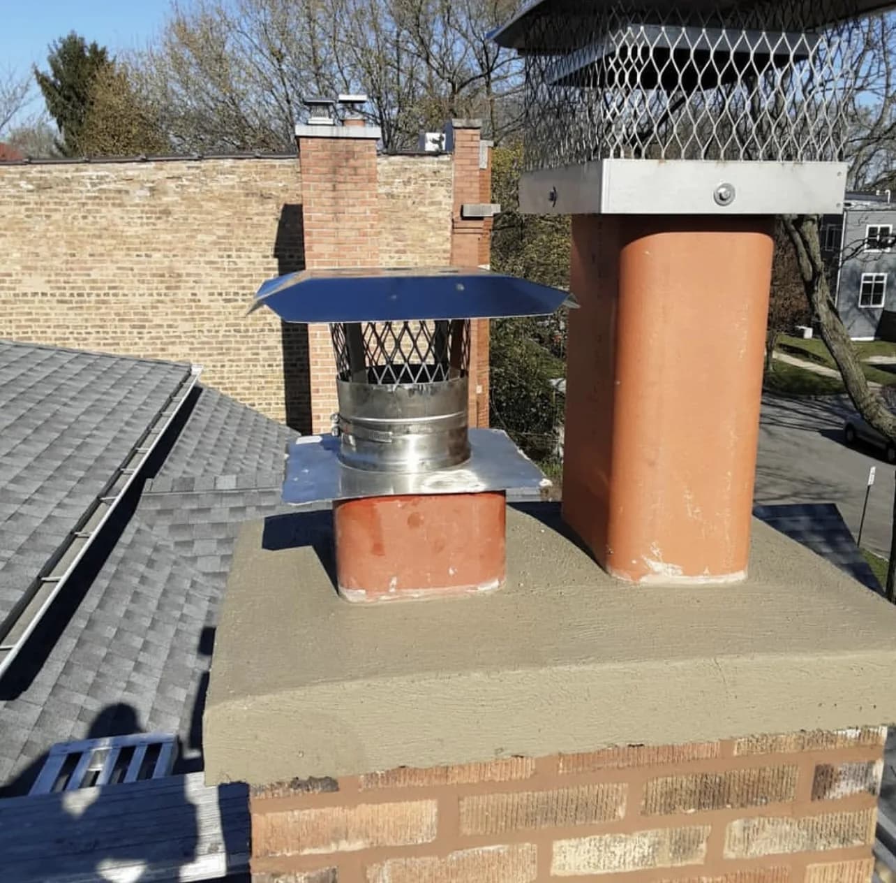 Brick chimney with a new stainless steel cap and freshly parged crown mortar on a New Jersey roof